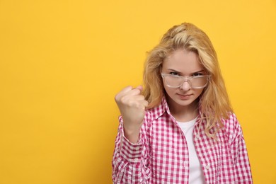 Photo of Aggressive young woman showing fist on yellow background. Space for text