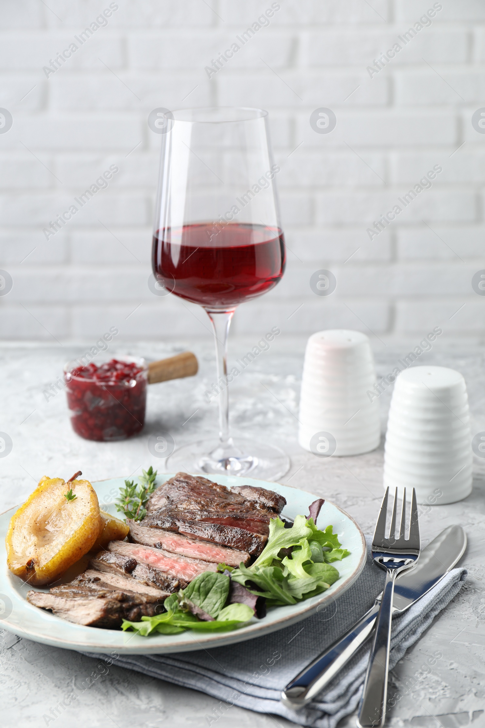 Photo of Delicious roasted beef meat, caramelized pear and greens served on light table