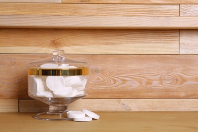 Composition of glass jar with cotton pads on table near wooden wall. Space for text