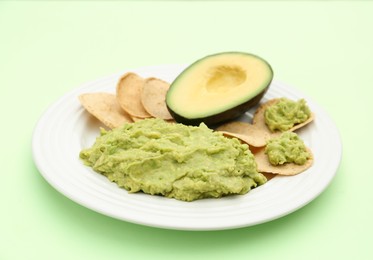 Photo of Delicious guacamole, avocado and chips on light green background