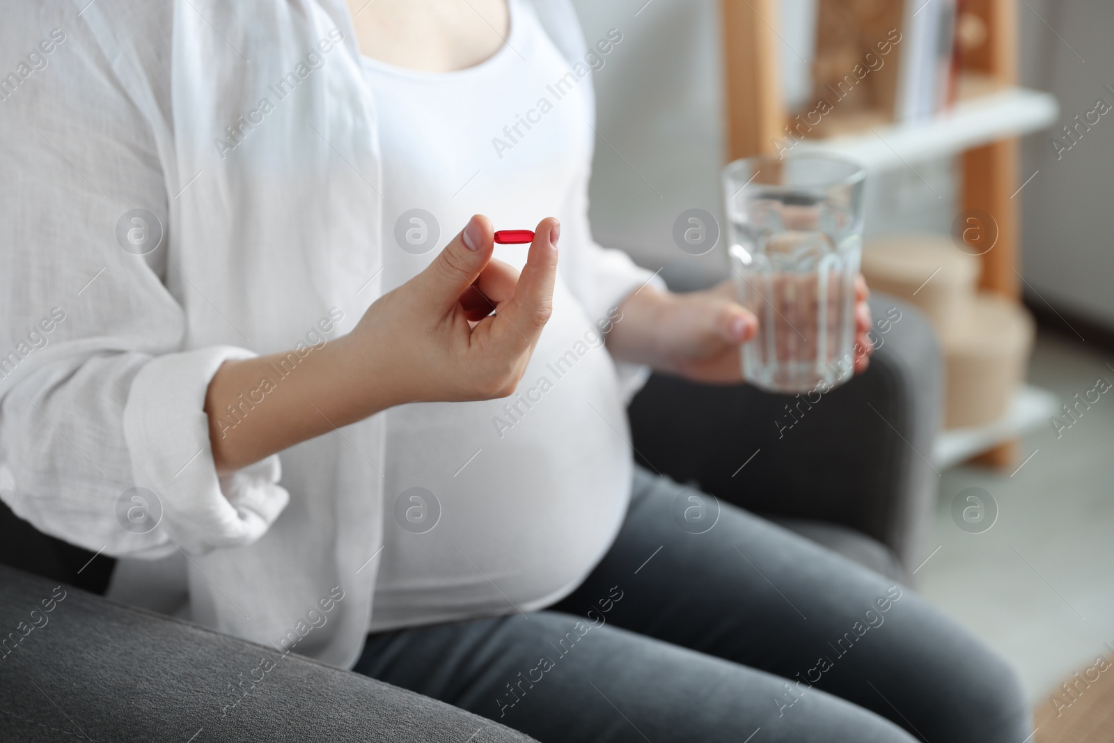 Photo of Pregnant woman holding pill and glass with water indoors, closeup
