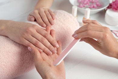 Photo of Manicurist filing client's nails at table, closeup. Spa treatment