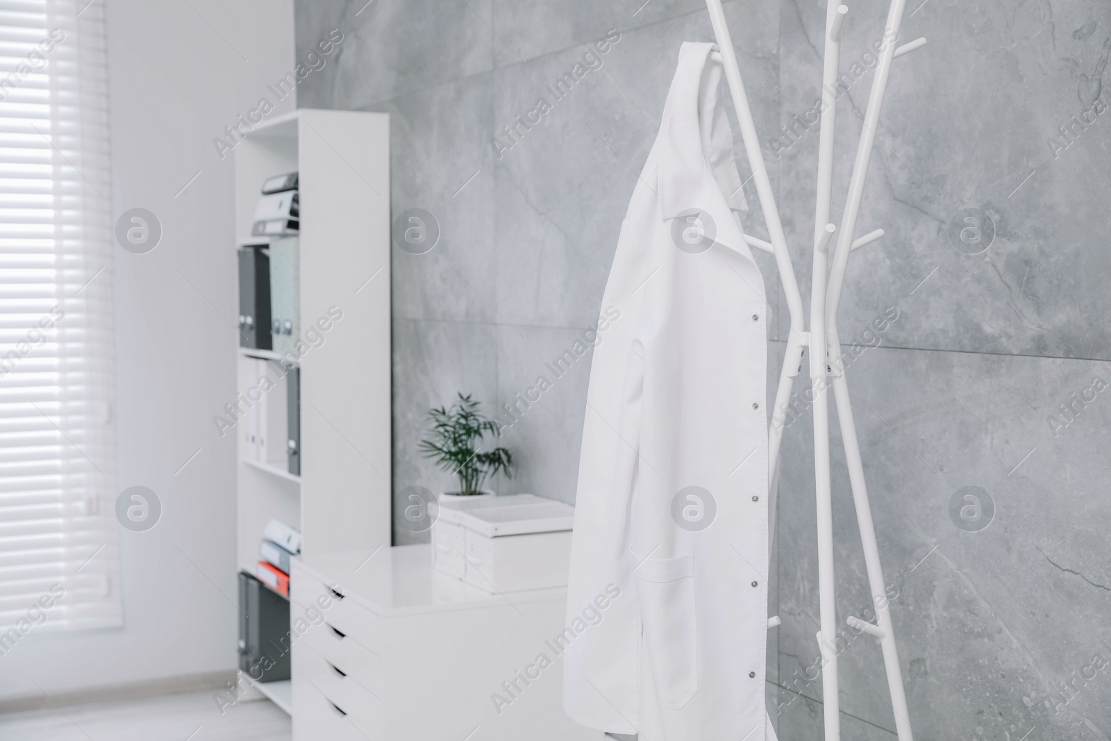 Photo of White doctor's gown hanging on rack in clinic. Space for text