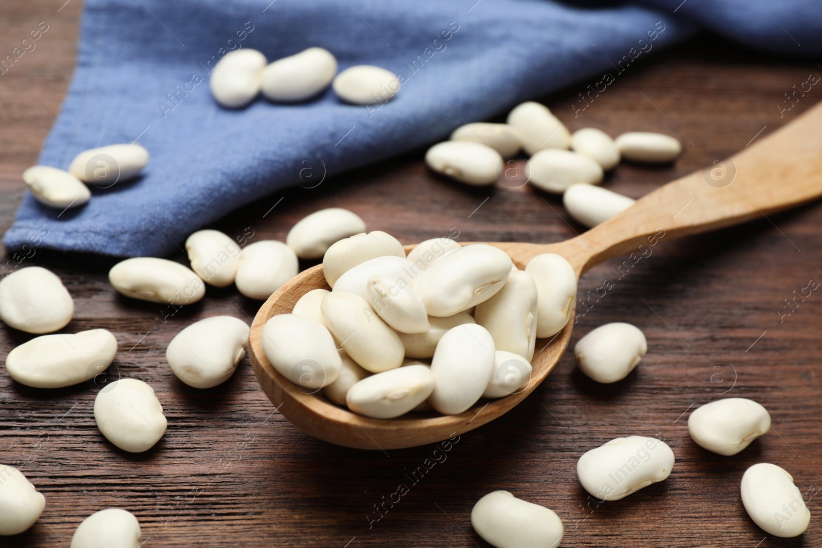 Photo of Raw white beans and spoon on wooden table, closeup