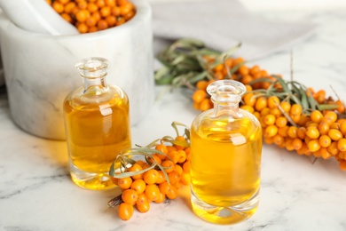 Photo of Natural sea buckthorn oil and fresh berries on white marble table