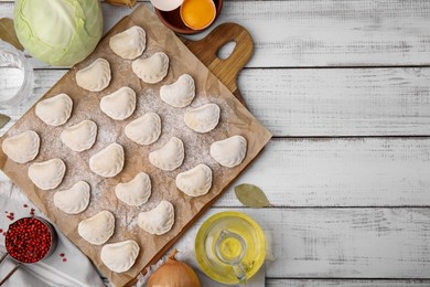 Photo of Raw dumplings (varenyky) with tasty filling and ingredients on white wooden table, flat lay. Space for text