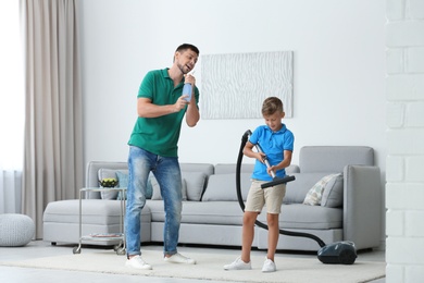Photo of Dad and son having fun while cleaning living room together