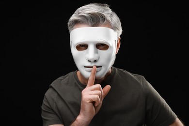 Man in mask showing hush gesture against black background