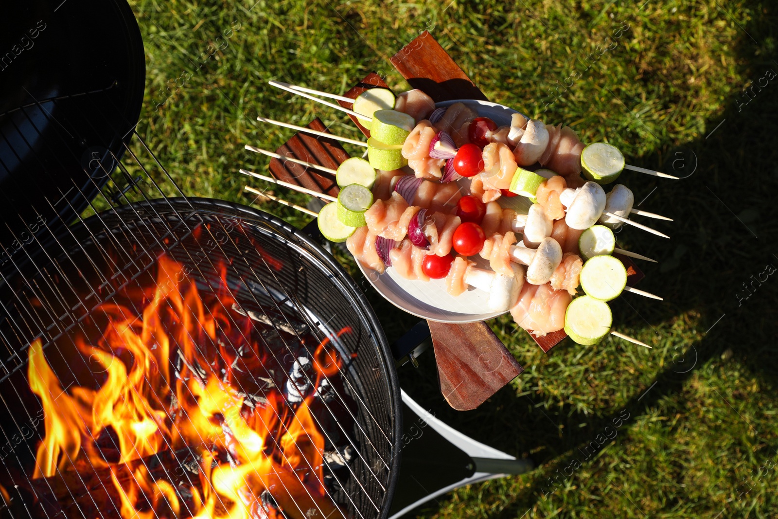 Photo of Skewers with meat and vegetables near barbecue grill outdoors, top view