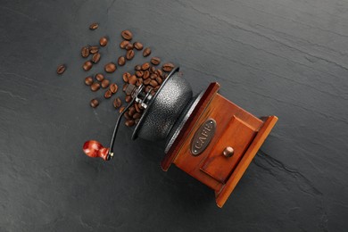 Photo of Vintage manual coffee grinder with beans on black table, flat lay