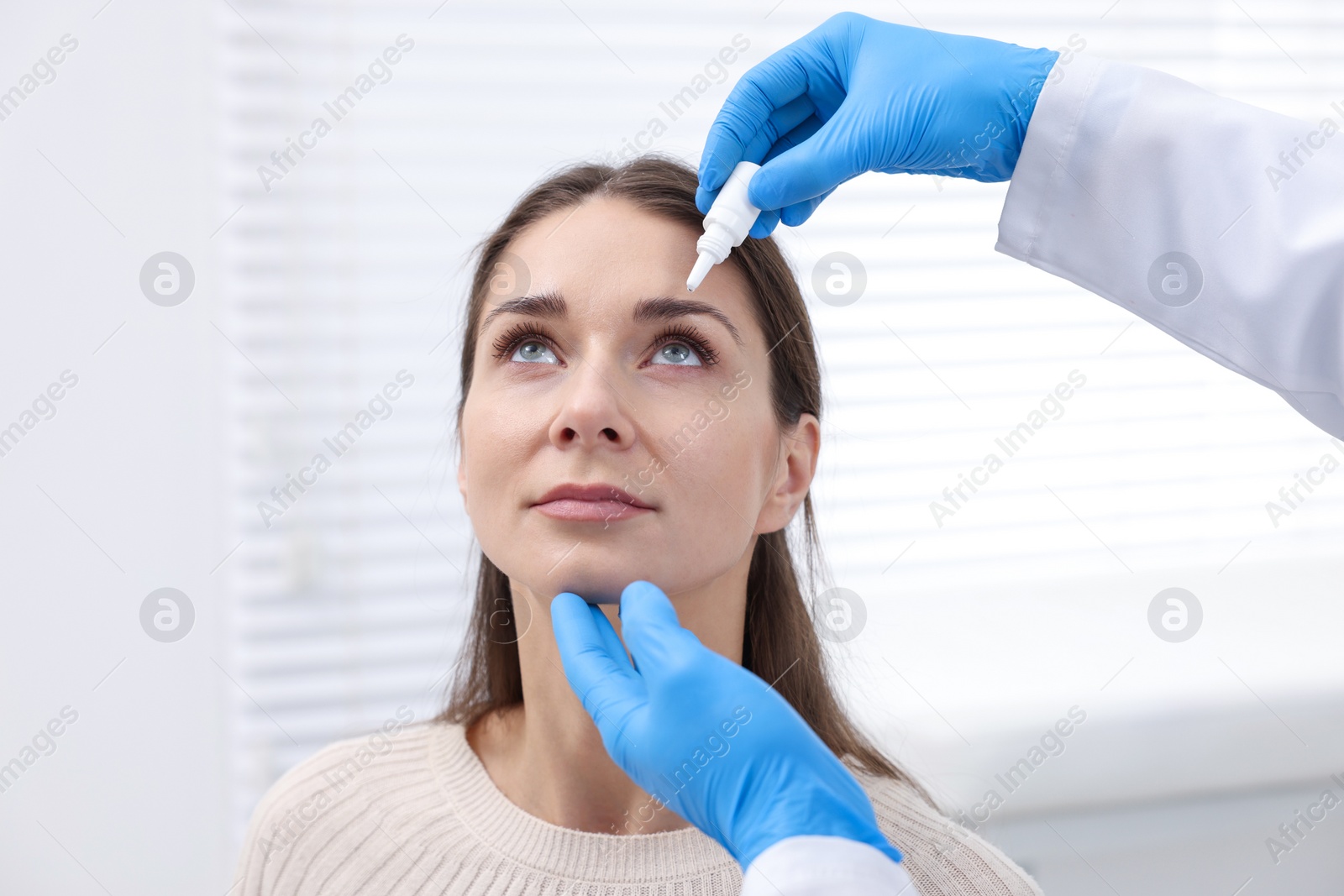 Photo of Doctor applying medical drops into woman's eye indoors