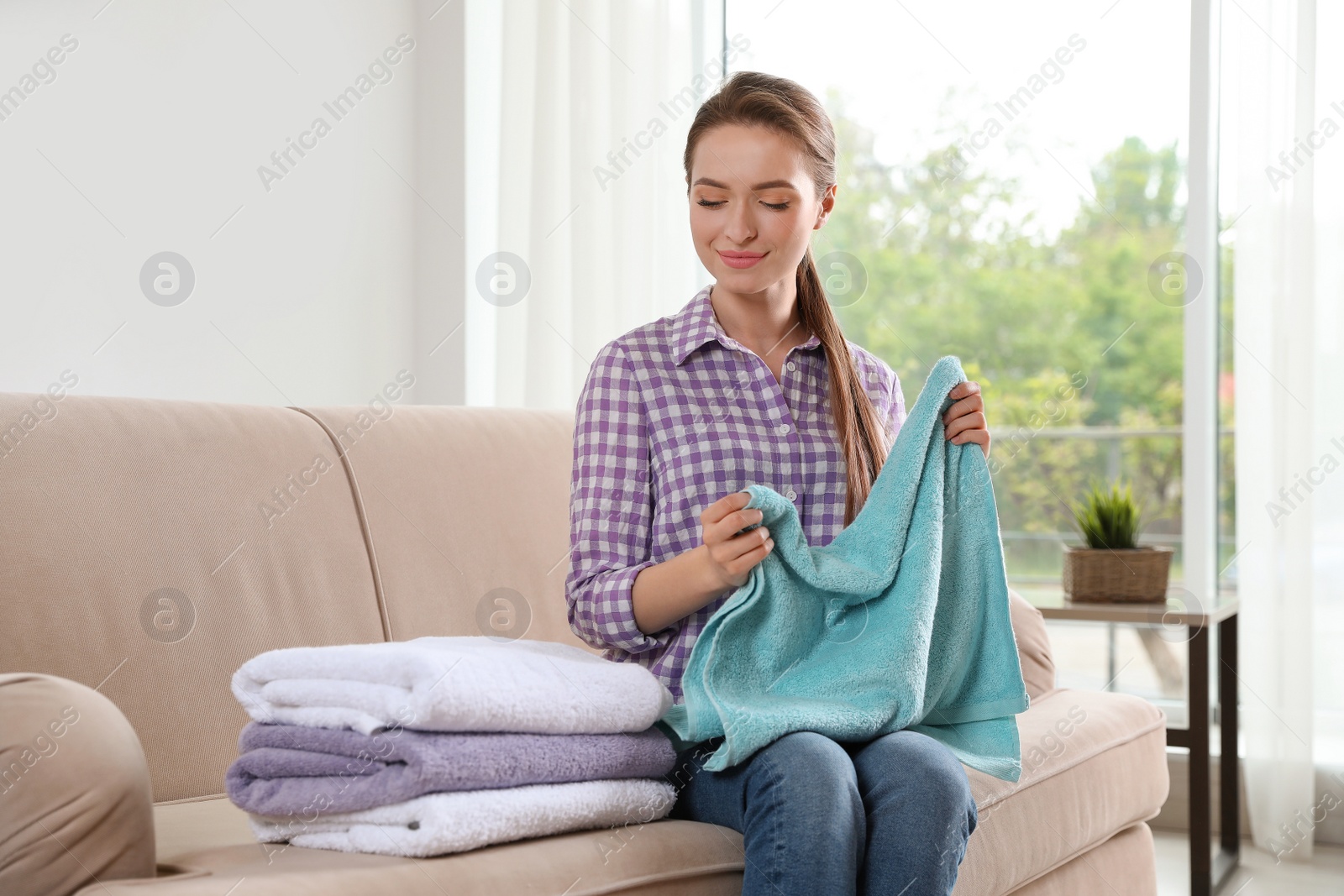 Photo of Young woman with clean laundry on sofa in room