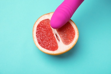 Photo of Half of grapefruit and purple vibrator on turquoise background, above view. Sex concept