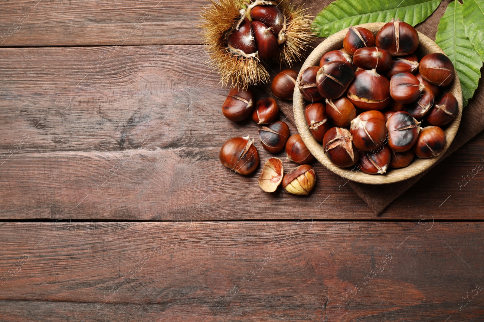 Photo of Delicious roasted edible chestnuts on brown wooden table, flat lay. Space for text