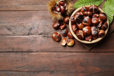 Delicious roasted edible chestnuts on brown wooden table, flat lay. Space for text