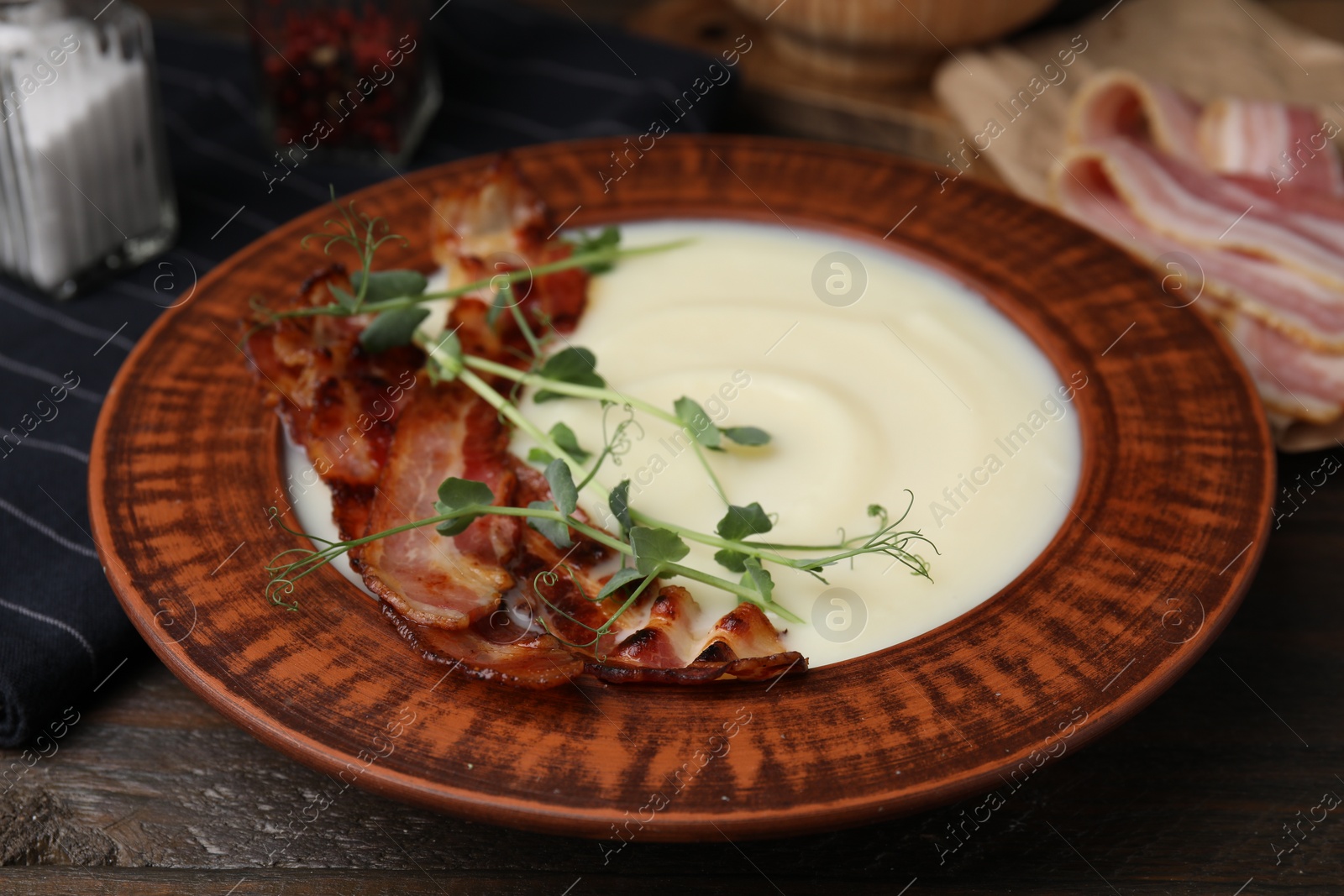 Photo of Delicious potato soup with bacon and microgreens in bowl on wooden table, closeup