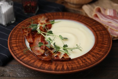 Photo of Delicious potato soup with bacon and microgreens in bowl on wooden table, closeup