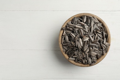 Photo of Raw sunflower seeds in bowl on white wooden table, top view. Space for text