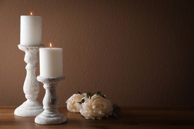Photo of Elegant candlesticks with burning candles and flowers on wooden table. Space for text