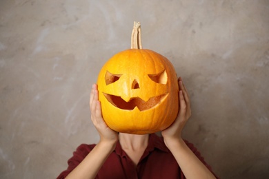 Woman with pumpkin head against beige background. Jack lantern - traditional Halloween decor