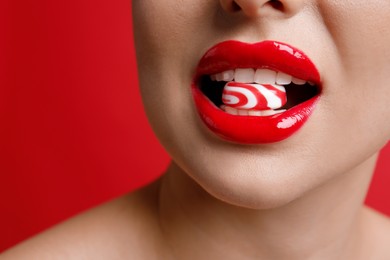 Photo of Closeup view of woman with beautiful lips eating candy on red background. Space for text
