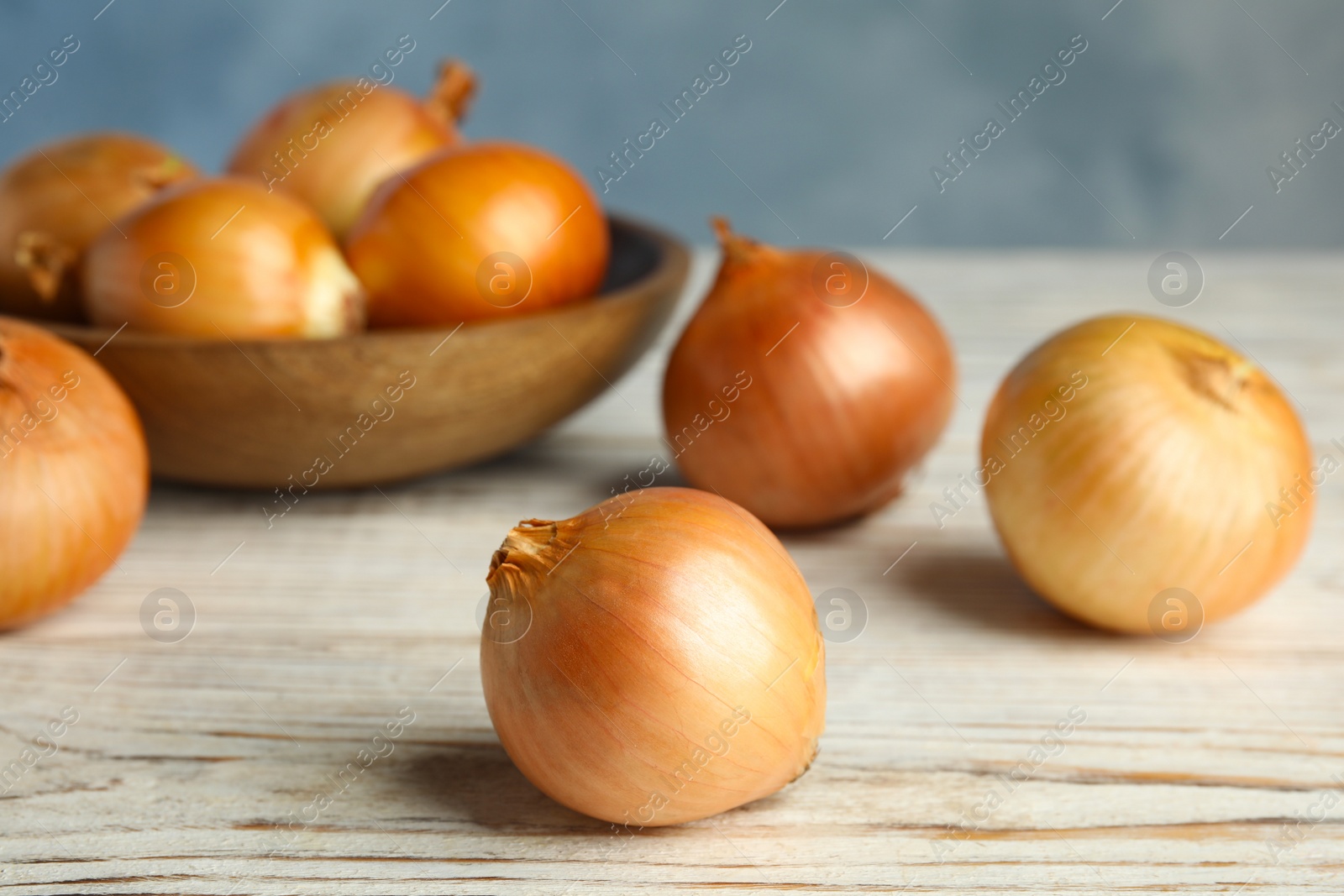 Photo of Ripe onions on white wooden table, closeup