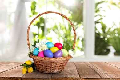 Image of Wicker basket with bright painted Easter eggs and spring flowers on wooden table