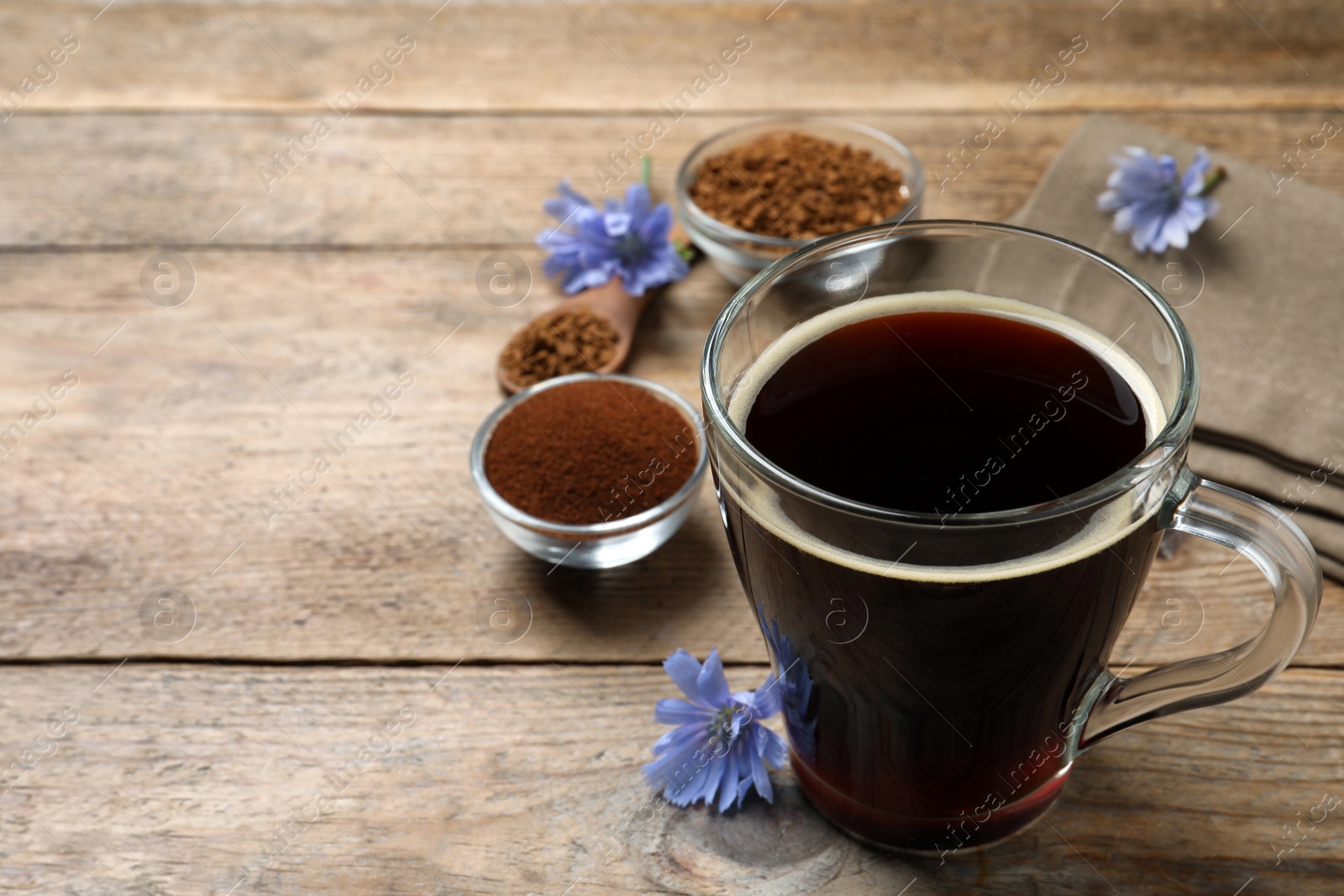 Photo of Glass cup of delicious chicory drink and flowers on wooden table. Space for text