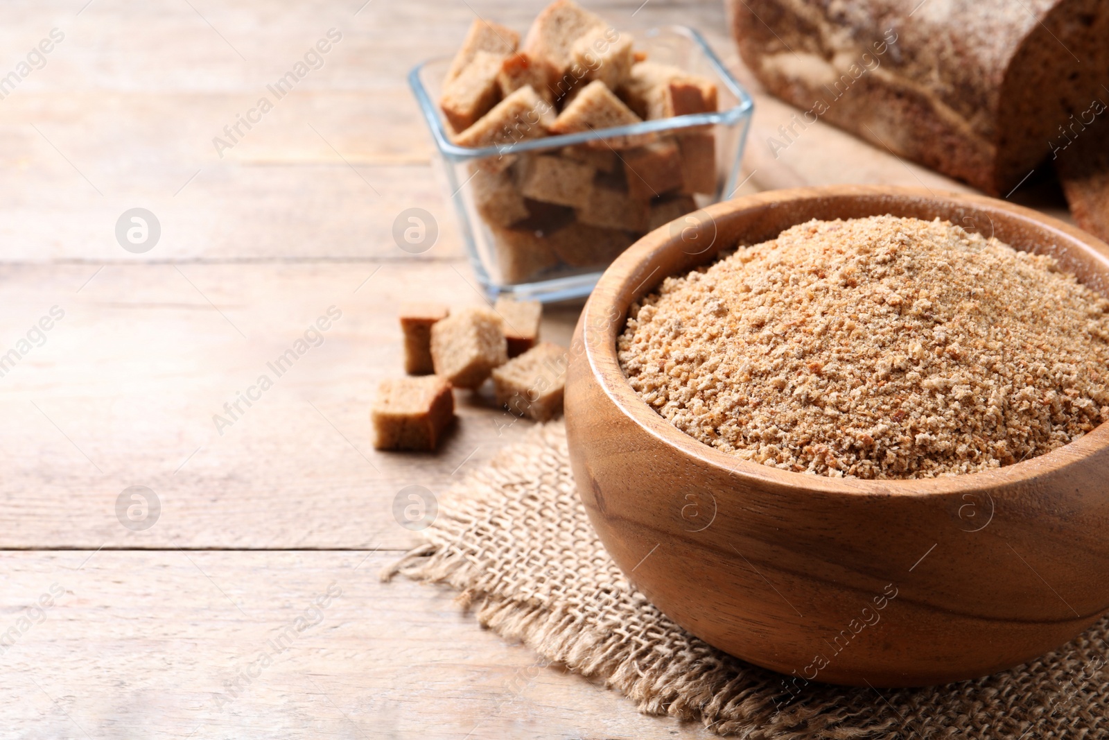 Photo of Fresh breadcrumbs in bowl on wooden table. Space for text