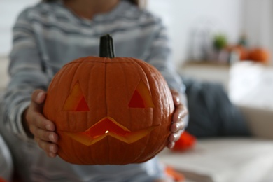 Photo of Woman holding pumpkin jack o'lantern indoors, closeup with space for text. Halloween celebration