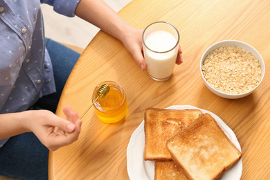 Photo of Woman with honey, milk, toasts and oatmeal at table, above view