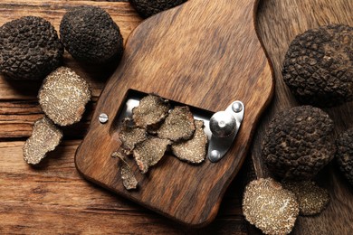 Photo of Shaver with whole and sliced black truffles on wooden table, flat lay