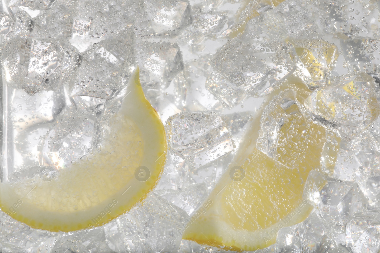 Photo of Juicy lemon slices and ice cubes in soda water against white background, closeup