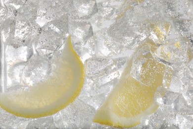 Photo of Juicy lemon slices and ice cubes in soda water against white background, closeup