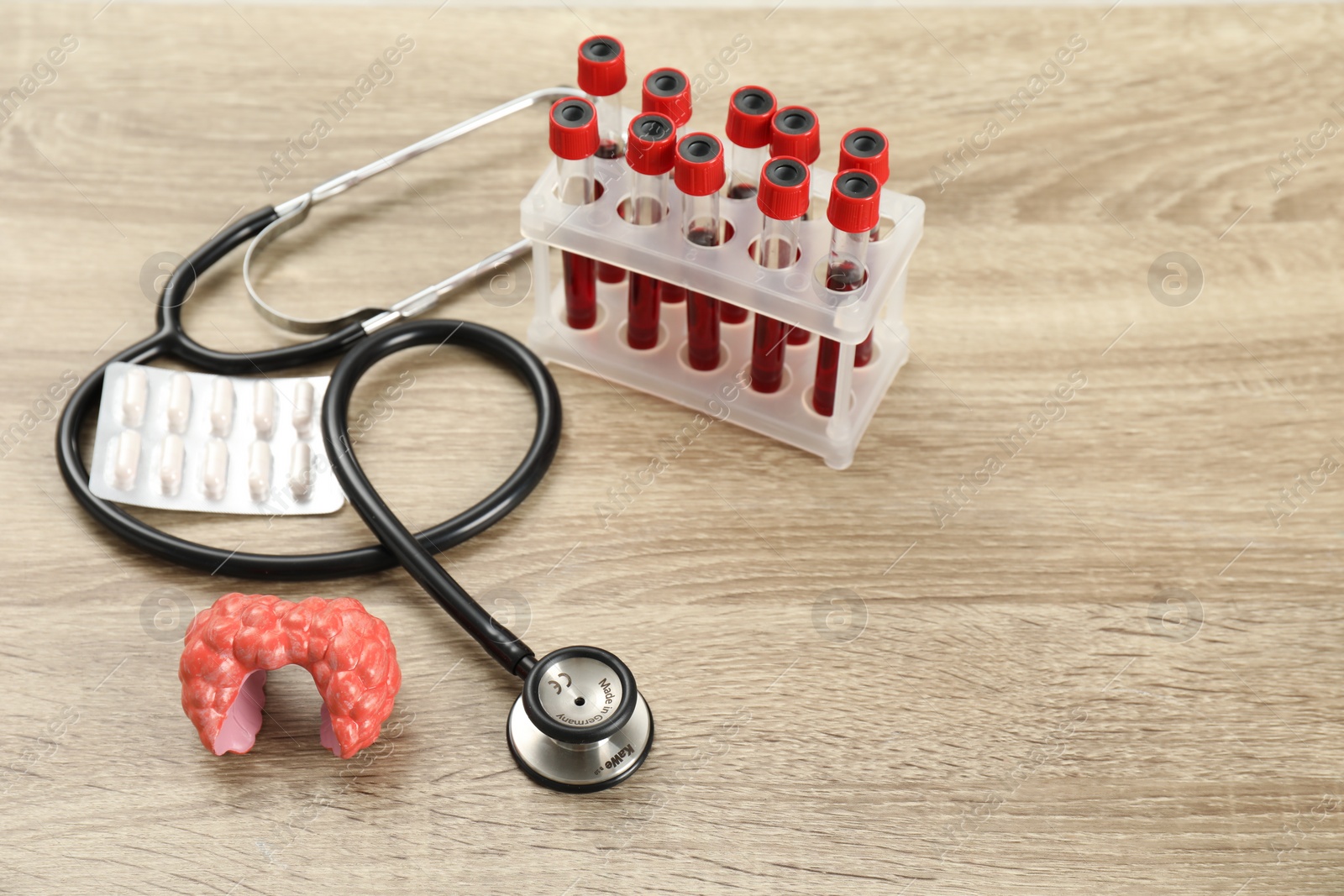 Photo of Endocrinology. Stethoscope, model of thyroid gland, pills and blood samples in test tubes on wooden table. Space for text