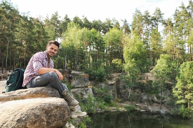 Photo of Young man on rock near lake and forest. Camping season