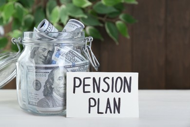 Photo of Card with phrase Pension Plan and dollar banknotes in glass jar on white wooden table. Retirement concept