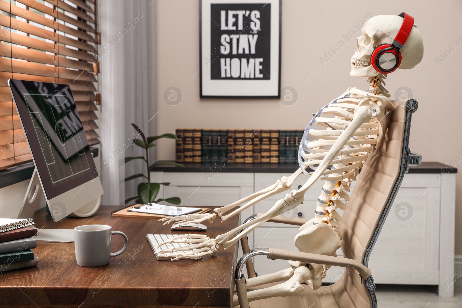 Photo of Human skeleton with headphones using computer at workplace