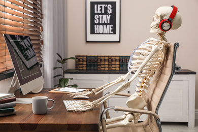 Photo of Human skeleton with headphones using computer at workplace