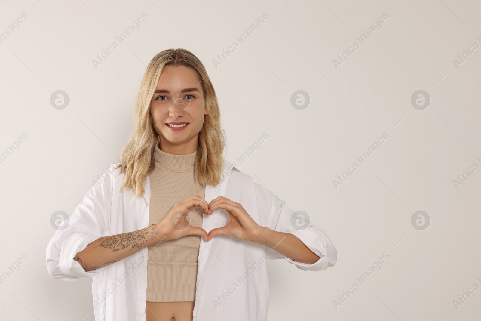 Photo of Happy volunteer making heart with her hands on light background. Space for text