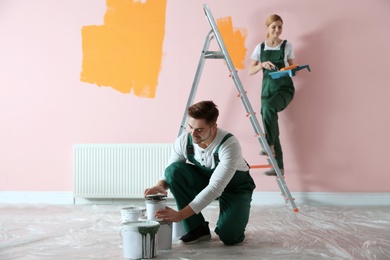 Photo of Professional decorators painting wall indoors. Home repair service