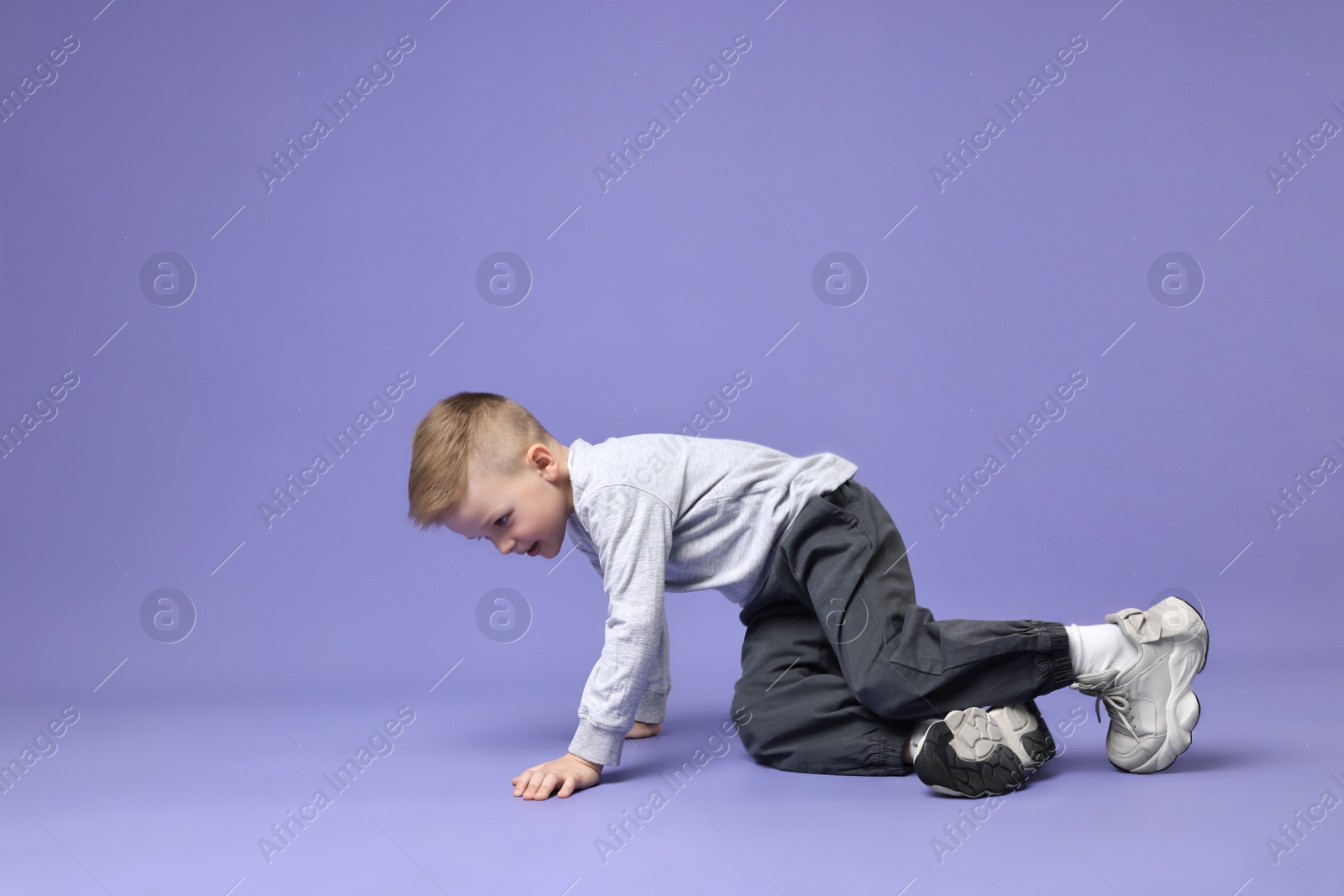 Photo of Happy little boy dancing on violet background