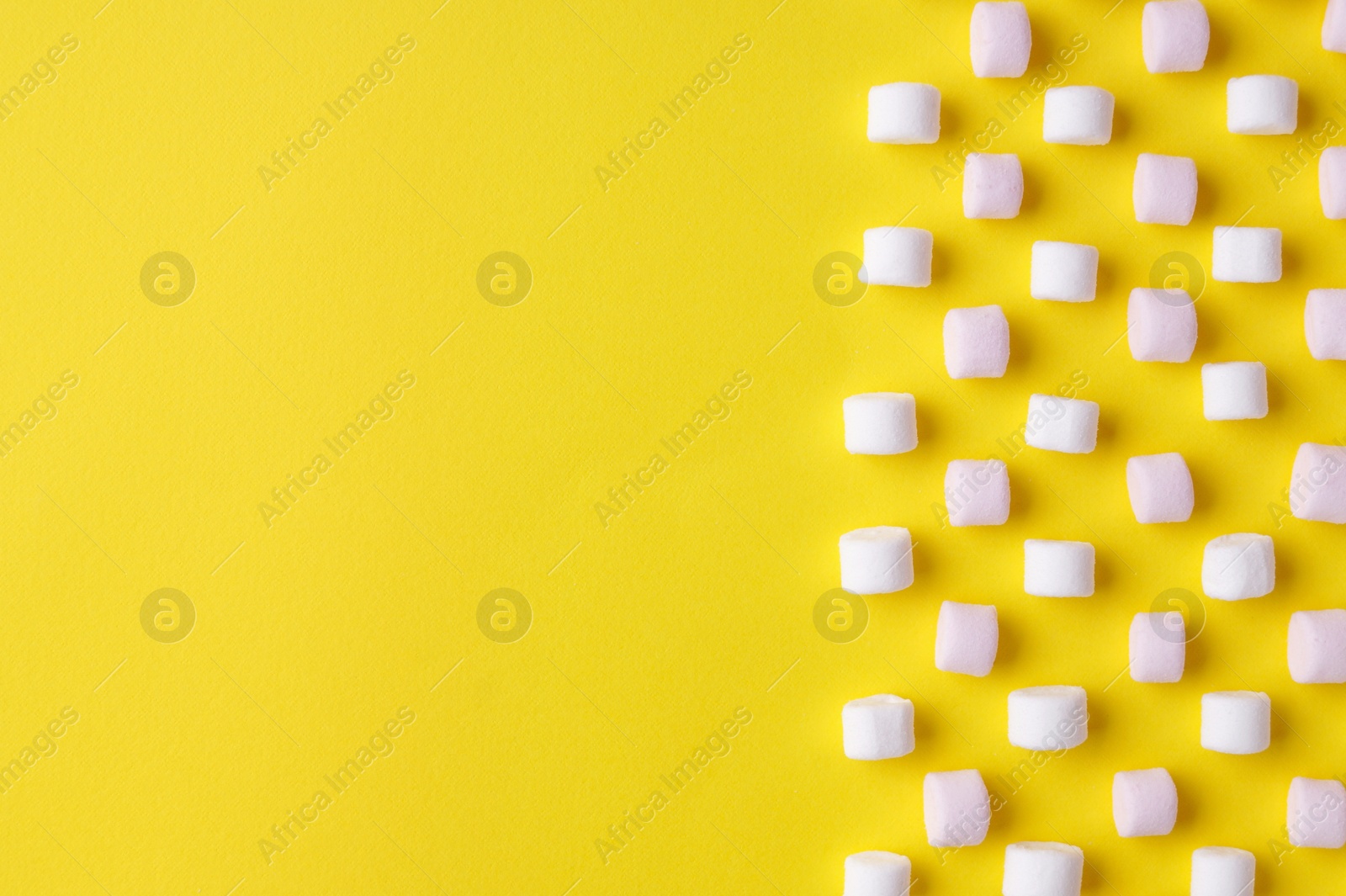 Photo of Delicious puffy marshmallows on yellow background, flat lay. Space for text