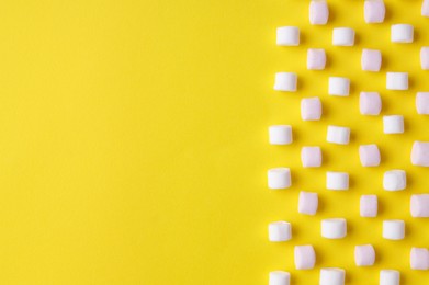 Photo of Delicious puffy marshmallows on yellow background, flat lay. Space for text