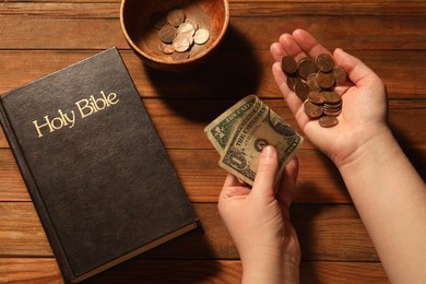 Donate and give concept. Woman with money, closeup. Bible and bowl of coins on wooden table, top view