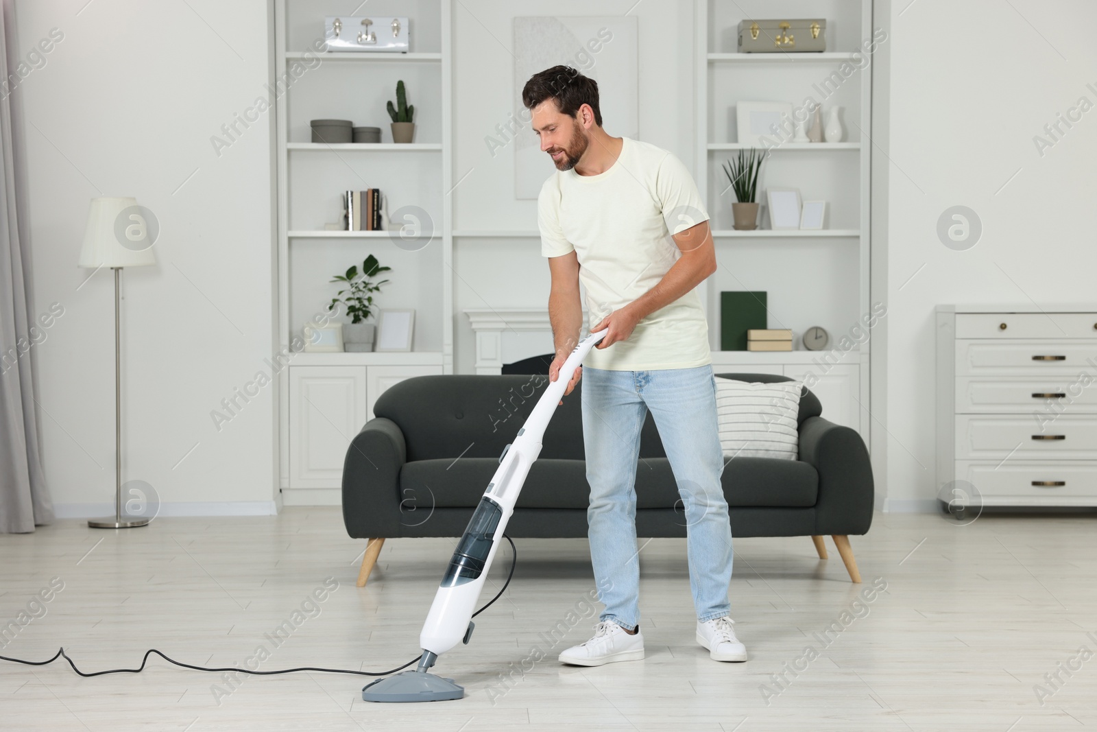 Photo of Happy man cleaning floor with steam mop at home