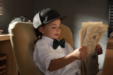 Photo of Cute little detective reading newspaper in office