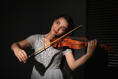 Photo of Beautiful young woman playing violin in dark room