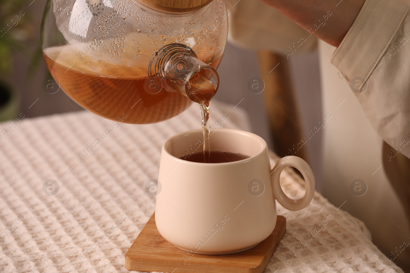 Photo of Woman pouring aromatic tea into cup at table, closeup