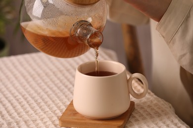 Woman pouring aromatic tea into cup at table, closeup